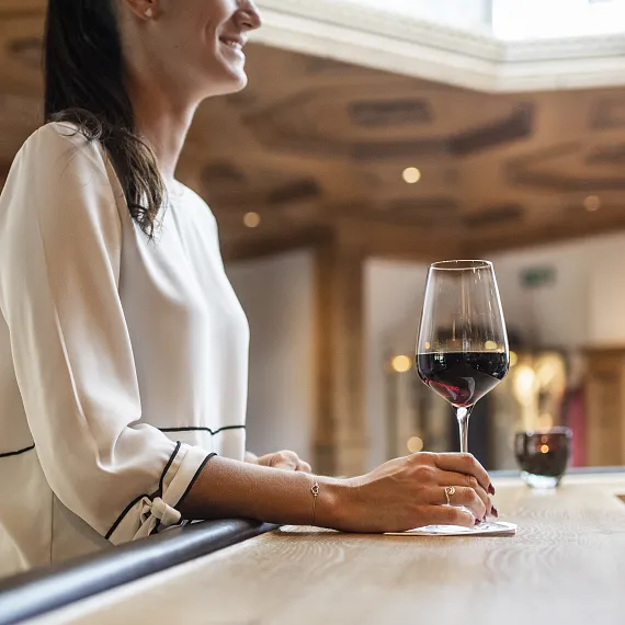 Frau in hellem Oberteil sitzt an einer Bar und hält ein Glas Rotwein, moderne Inneneinrichtung.