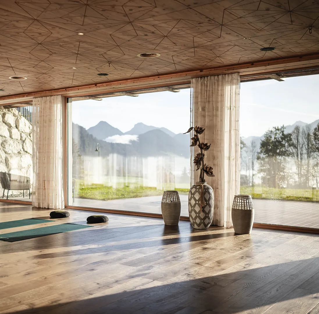 Moderner, heller Raum mit Bergblick, Holzboden und großen Fenstern, Dekovasen im Vordergrund.