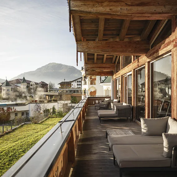 Bergblick von einer Holzveranda in Tirol mit modernen Gebäuden und einem großen Berg im Hintergrund.
