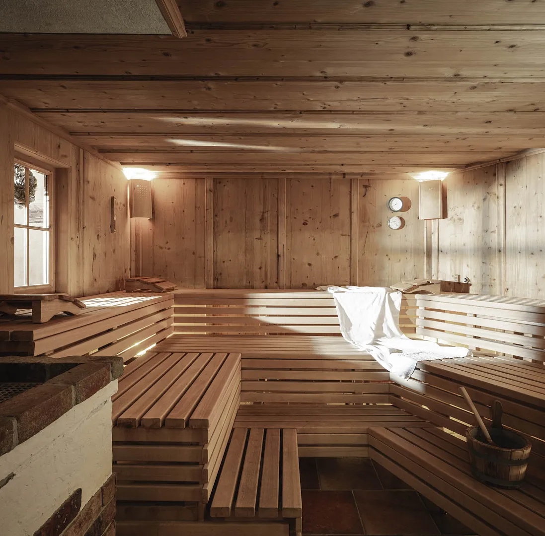 Leere Holzsauna mit Bänken, einem Saunaeimer und Handtüchern auf der linken Bank, warm beleuchtet.