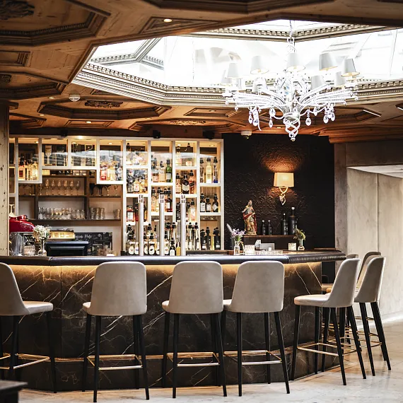 Elegante Bar mit modernen Stühlen, beleuchteten Regalen voller Flaschen und einem Kronleuchter, wahrscheinlich in einem Hotel.
