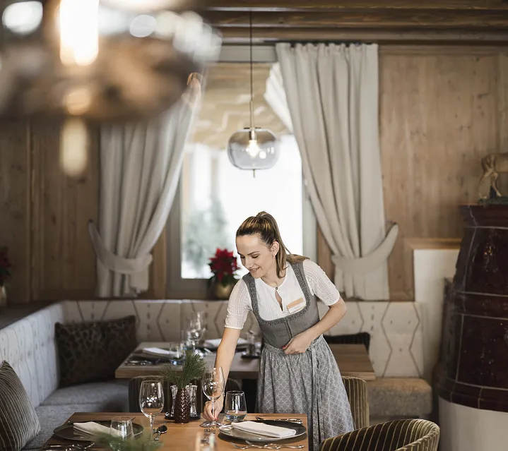 Frau im dirndl im Restaurant, arrangiert Tisch im traditionellen Alpenstil.