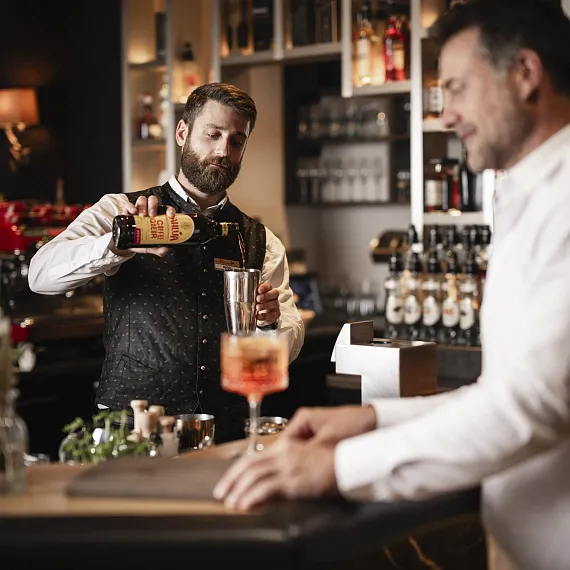 Bartender in Bar gießt Getränk ein, Gast wartet am Tresen.