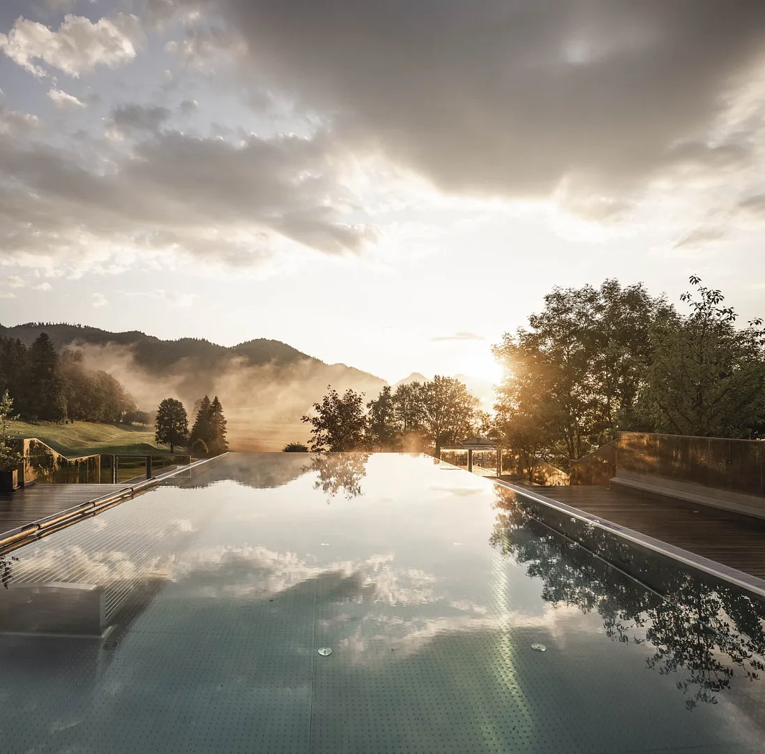 Infinity pool reflecting the sky and mountains at sunset in a tranquil landscape.