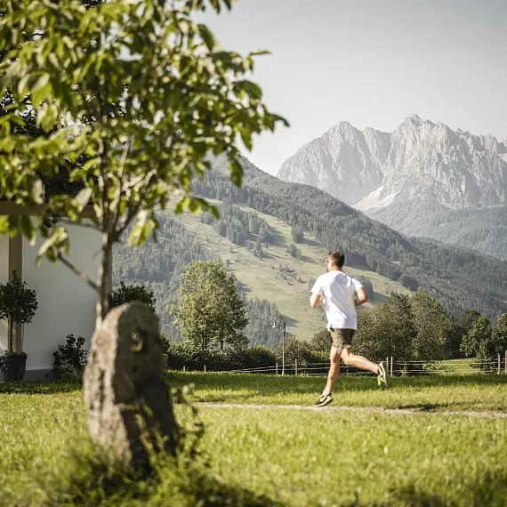 Läufer in Landschaft von Kitzbühel mit Bergen im Hintergrund, bei sonnigem Wetter, neben einem Gebäude.