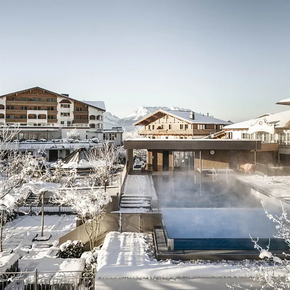 Verschneite Hotelanlage in Kitzbühel mit offenem Winterpool, umgeben von Schnee und klarer Winterluft.