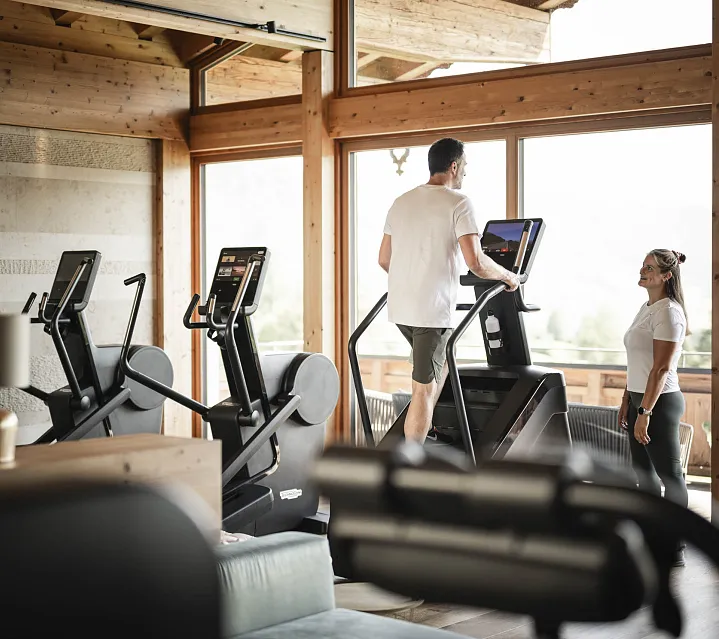Personen trainieren in einem modernen Fitnessraum mit Holzdesign und großen Fenstern.