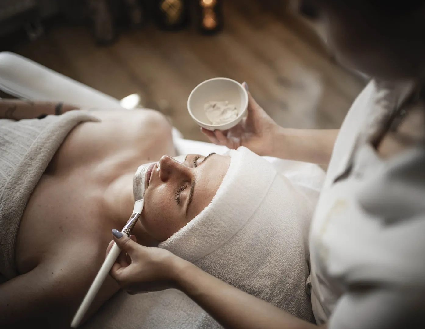Person in einem Spa erhält eine Gesichtsmaske von einer Kosmetikerin aufgetragen.