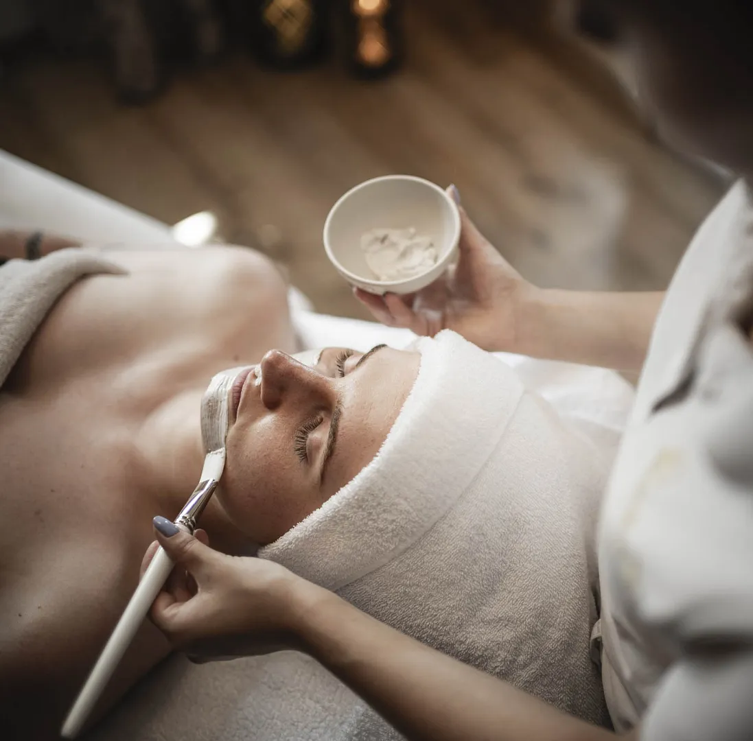 Person in einem Spa erhält eine Gesichtsmaske von einer Kosmetikerin aufgetragen.
