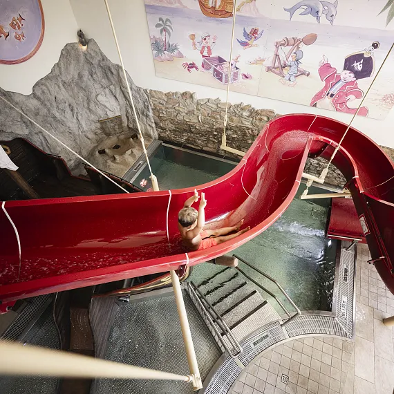 Kind rutscht in roter Tunnelrutsche in einem Indoor-Wasserpark.
