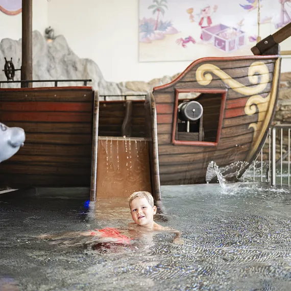 Kind schwimmt im Freizeitpark-Pool mit Piratenschiffsdekoration und Skulptur eines Seehunds.