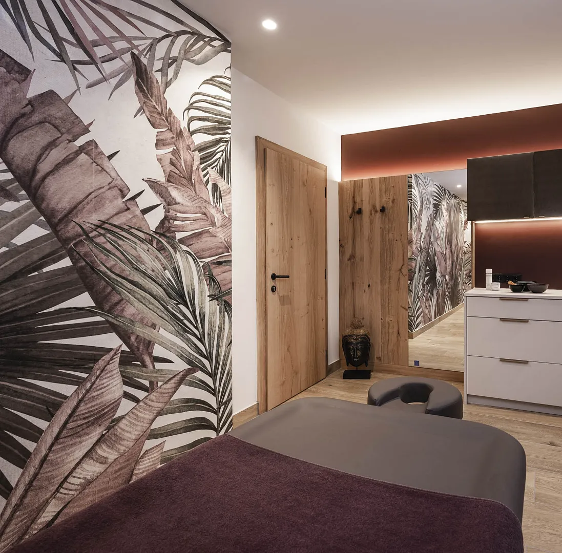Modernes Spa-Interieur mit Massageliege, Holzakzenten und großem Blattmotiv an der Wand.