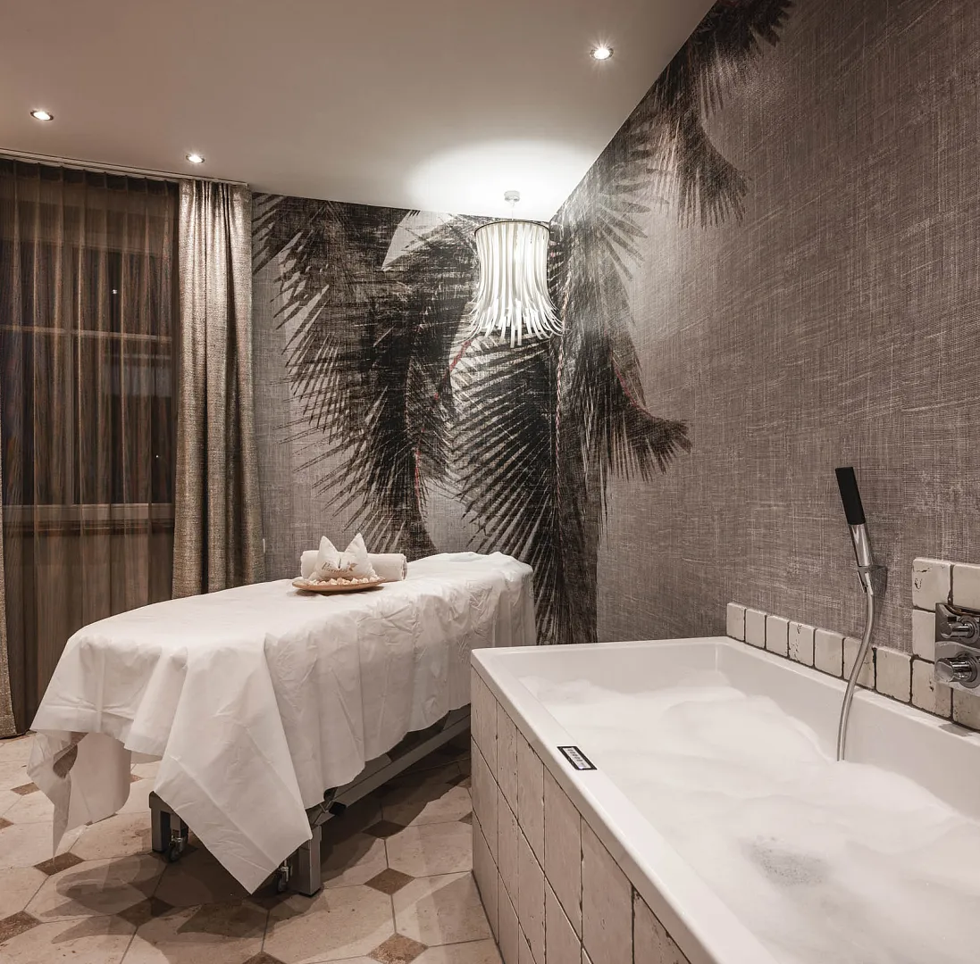 Wellnessraum mit Massageliege, Badewanne und neutraler Dekoration in warmen Tönen.