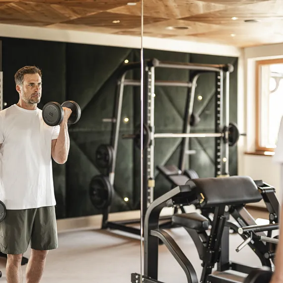 Mann im Fitnessstudio hebt Hantel vor einem Spiegel.
