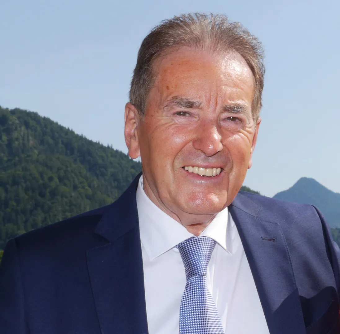 A man in a suit with a mountainous landscape in the background.