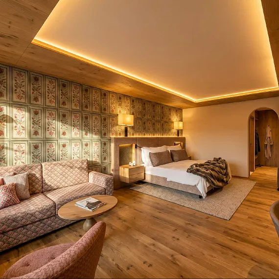 Zimmer in Tiroler Stil mit Holzelementen, Sofa, Doppelbett und dezenter Beleuchtung.