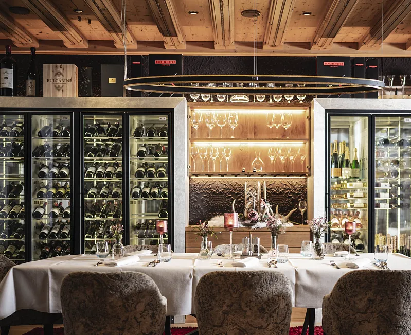 Elegantes Restaurantinterieur mit gedecktem Tisch und einer Wand mit Weinflaschen und Gläsern beleuchtet in warmem Licht.