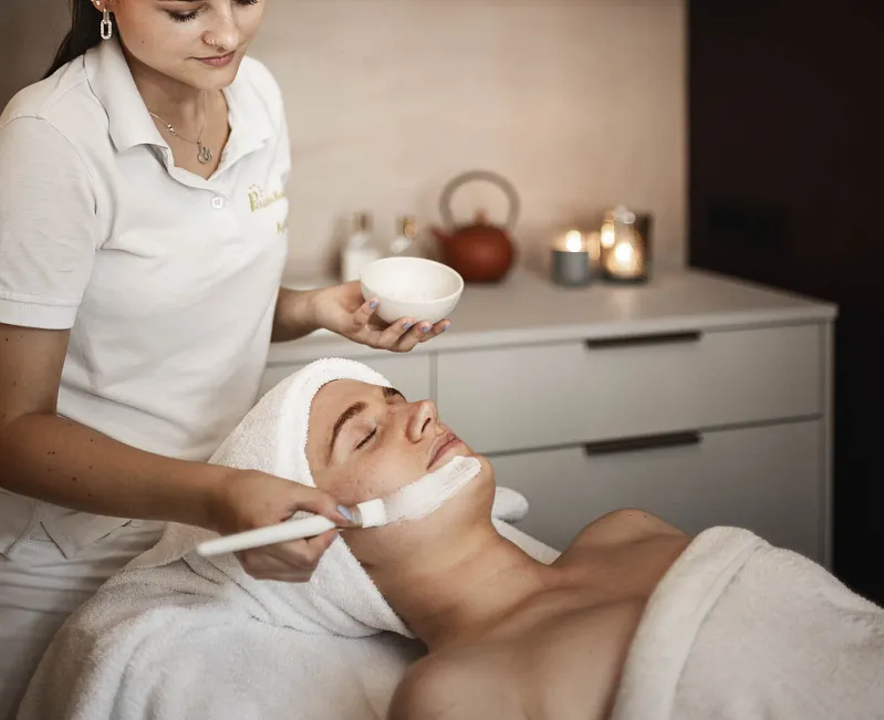 Kosmetikerin trägt Gesichtsmaske bei Kunde in einem Spa-Raum auf.