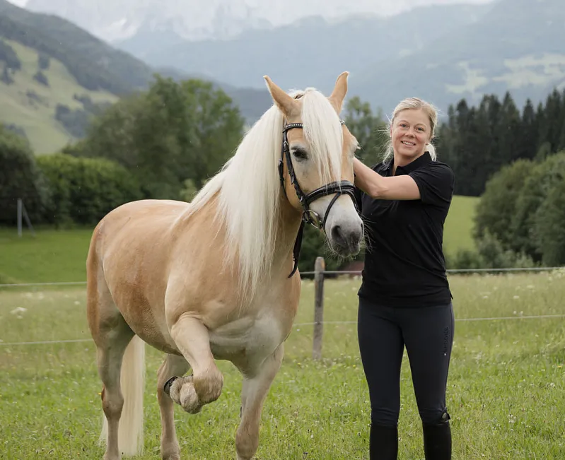 Frau steht mit einem Haflinger-Pferd auf einer Wiese in den Tiroler Alpen.