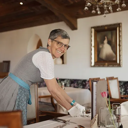 Eine lächelnde Person in traditioneller Kleidung richtet Tische in einem stilvollen Restaurant her.