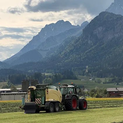 Traktor sammelt Heu vor Berglandschaft in Tirol.