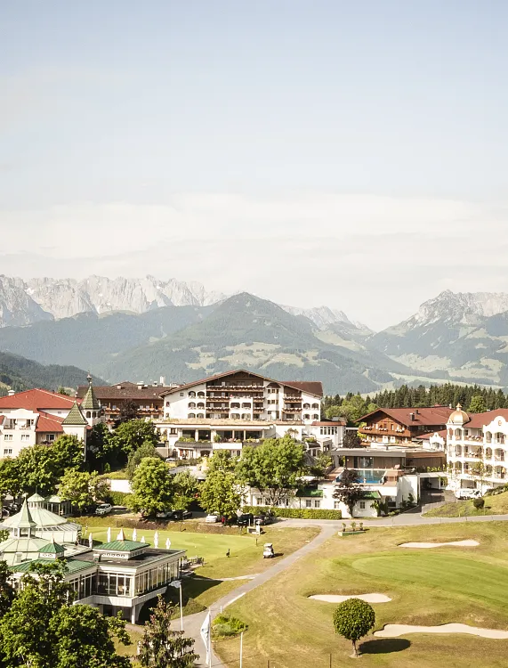 Berglandschaft mit Hotelkomplex in Kitzbühel, Tirol, im Vordergrund ein gepflegter Golfplatz.