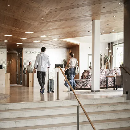 Hotel-Lobby mit Personen am Empfangsschalter, Holzdecke und Pflanzen, wahrscheinlich in Tirol.