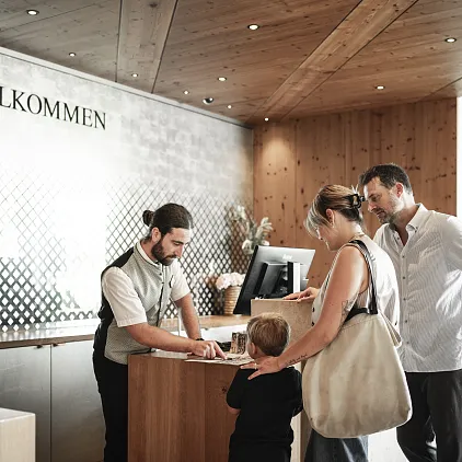 Rezeptionist in einem Hotel begrüßt eine Familie beim Check-in, moderner Empfangsbereich.