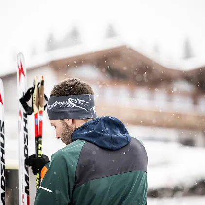 Person im Winteroutfit mit Langlaufskiern vor einem verschneiten Gebäude in Tirol.