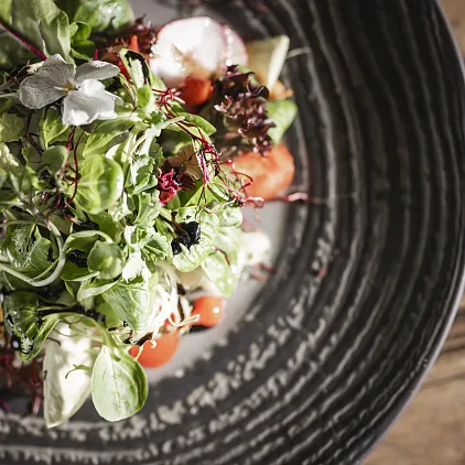 Frischer Salat mit einer Mischung aus grünen Blättern, Tomaten und Radieschen in einer schwarzen, strukturierten Schale.