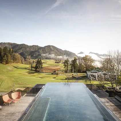 Infinity-Pool mit Blick auf eine Herbstlandschaft in Kitzbühel, umgeben von Bäumen und Bergen im Hintergrund.