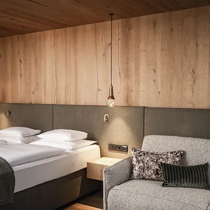 Modernes Hotelzimmer mit Holzwänden, Doppelbett und grauem Sofa in Tirol.