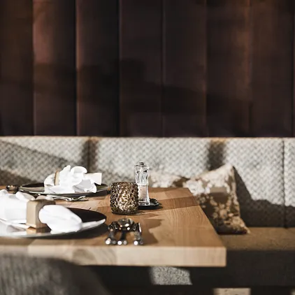 Eleganter Restauranttisch mit gefalteten Servietten, Kerze und Gewürzstreuer auf Holztisch, samtbezogene Sitzbank im Hintergrund.