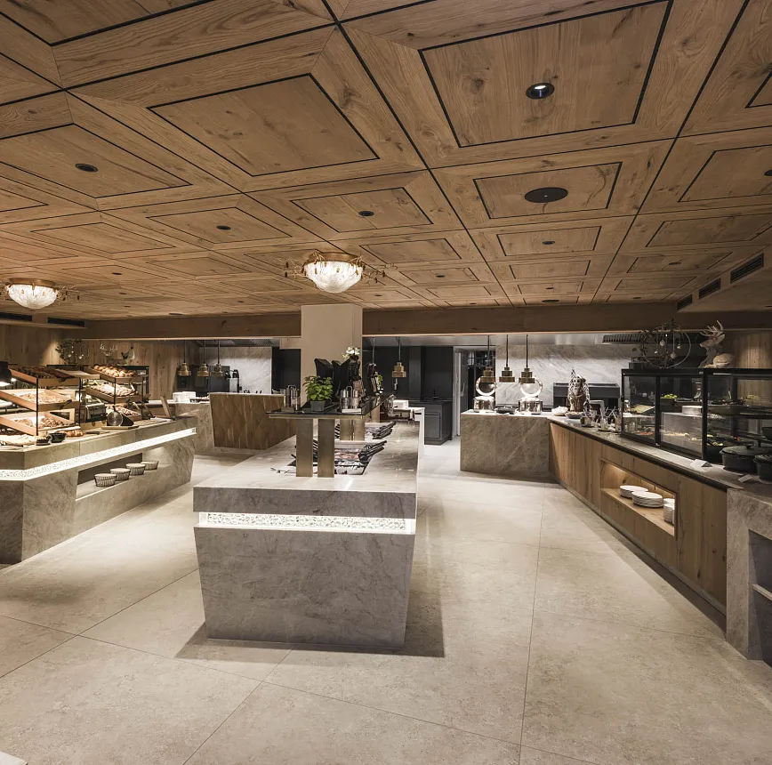 Moderner Speisesaal mit Holzdecke, Marmortischen und beleuchteten Buffets.