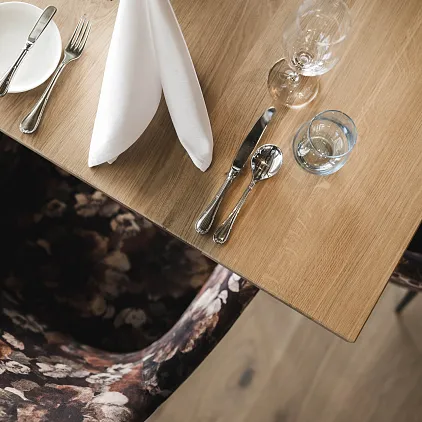 Holztisch mit elegant gedecktem Gedeck, Gläsern und Textilstühlen in Blumenmuster.