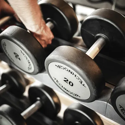 Person greift nach Hanteln in einem Fitnessstudio, umgeben von mehreren Gewichtsscheiben.