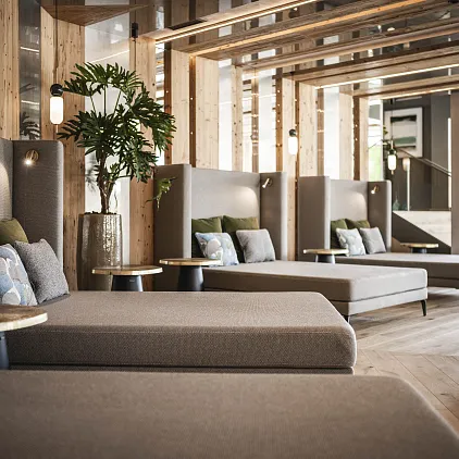 Lounge mit modernen grauen Sofas in einem stilvoll eingerichteten Raum, dahinter Holzverkleidungen und Pflanzen.