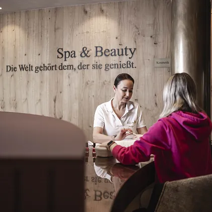 Eine Frau im Spa-Bereich spricht mit einer Kundin an einem Tisch.