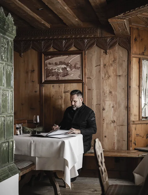 Mann in rustikalem Holzinterieur schreibt an einem Tisch mit einem Notizbuch.