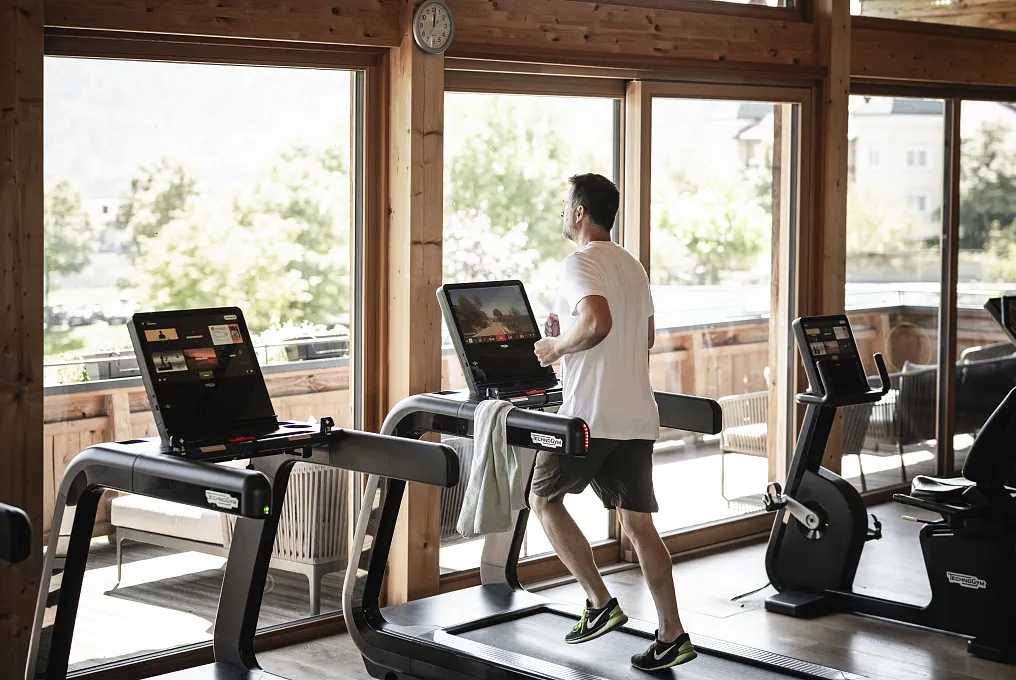 Mann läuft auf einem Laufband in einem hell erleuchteten Fitnessstudio mit großen Fenstern.