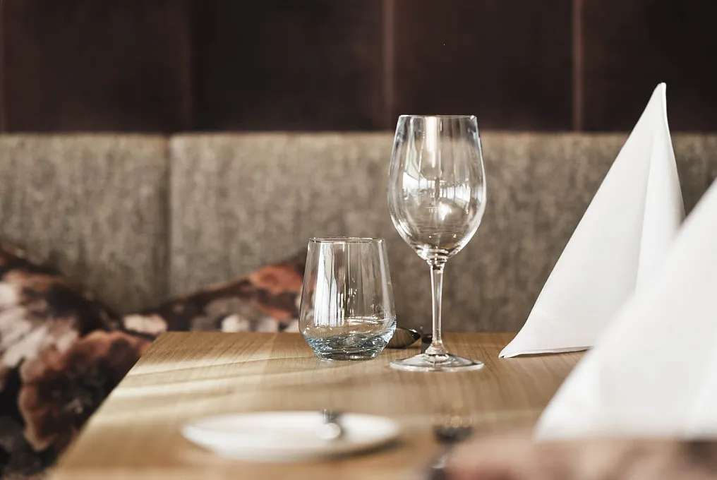 Leere Weingläser und ein Wasserglas auf einem Holztisch in einem eleganten Restaurantambiente.