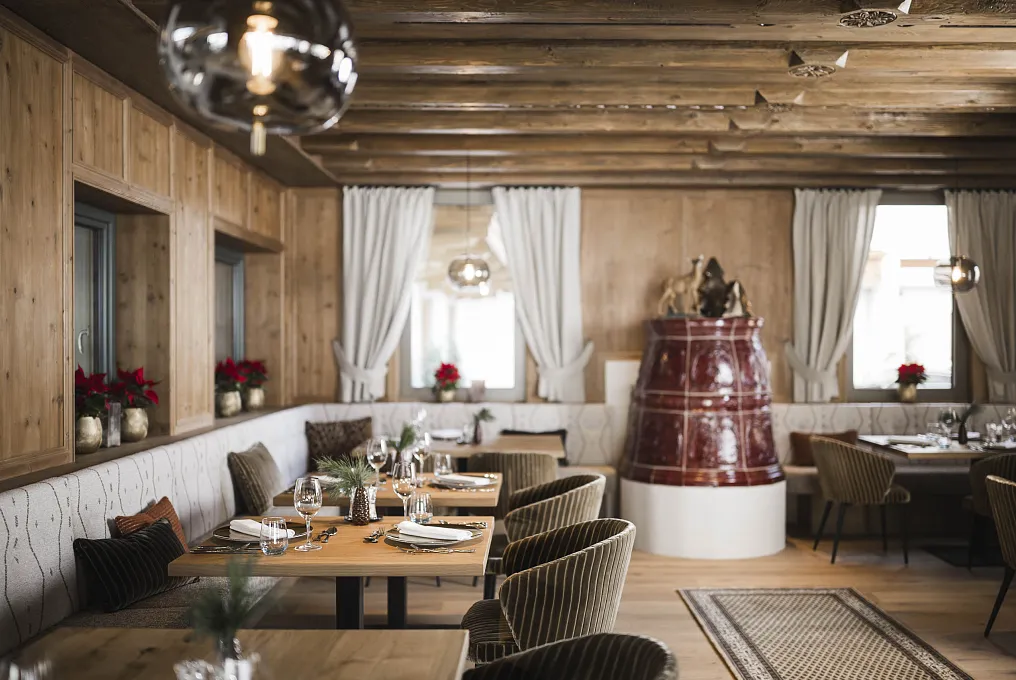 Gemütliches Restaurant in Tirol mit Holzwänden, Tischen aus Holz und einem roten Kachelofen.