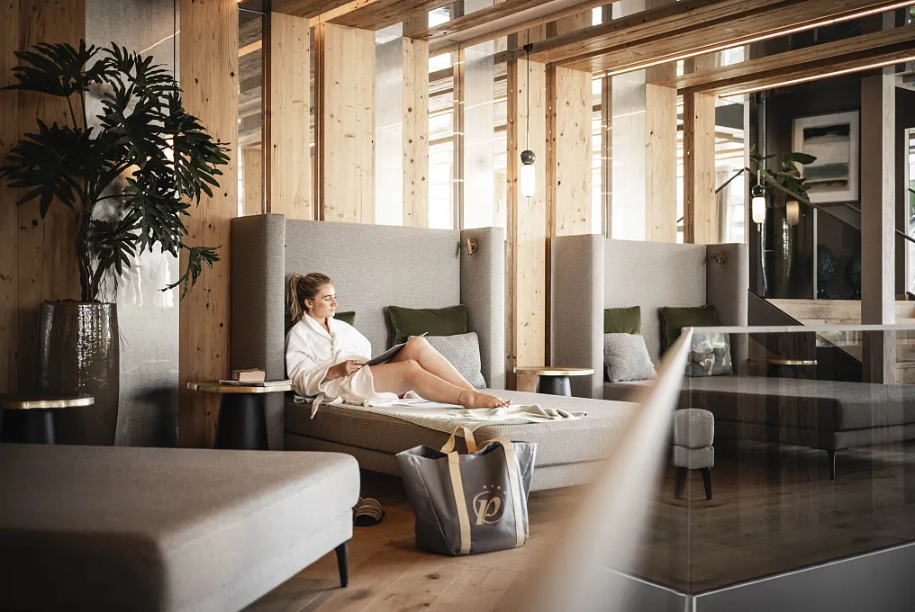 Person in Bademantel entspannt auf einer Liege in einem modernen Wellnessbereich aus Holz.