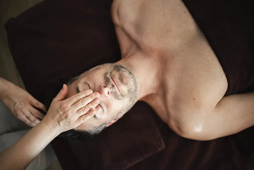 Person erhält Gesichtsmassage auf dunkler Liege.