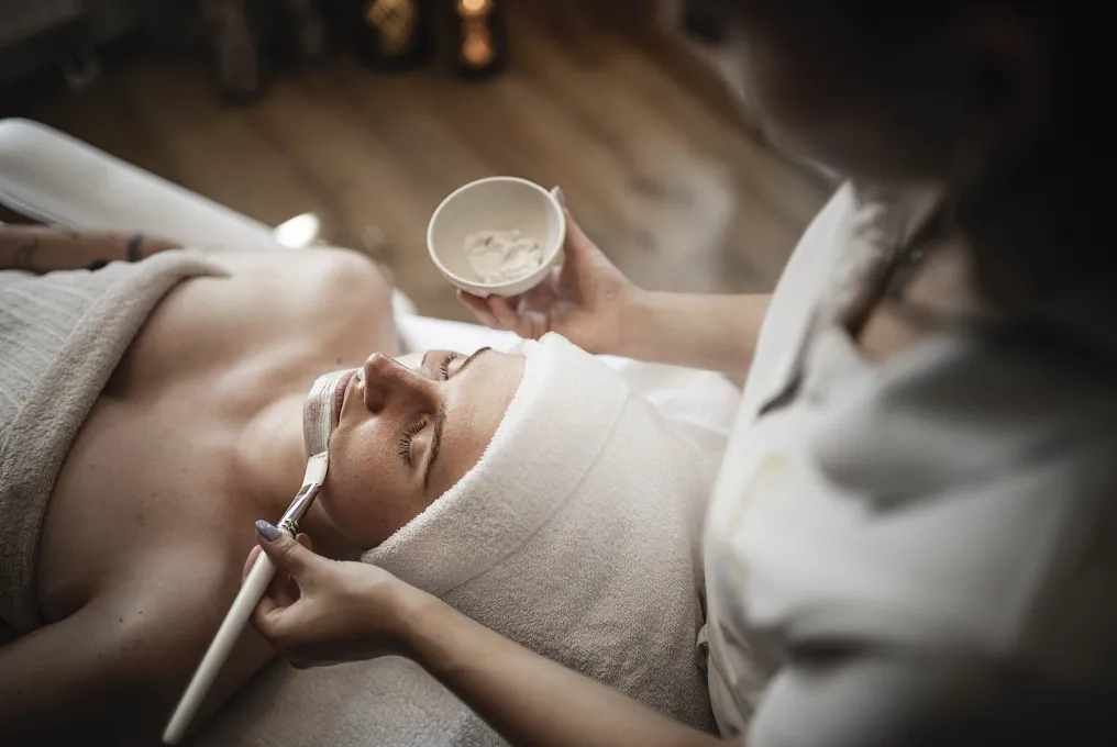 Person in einem Spa erhält eine Gesichtsmaske von einer Kosmetikerin aufgetragen.