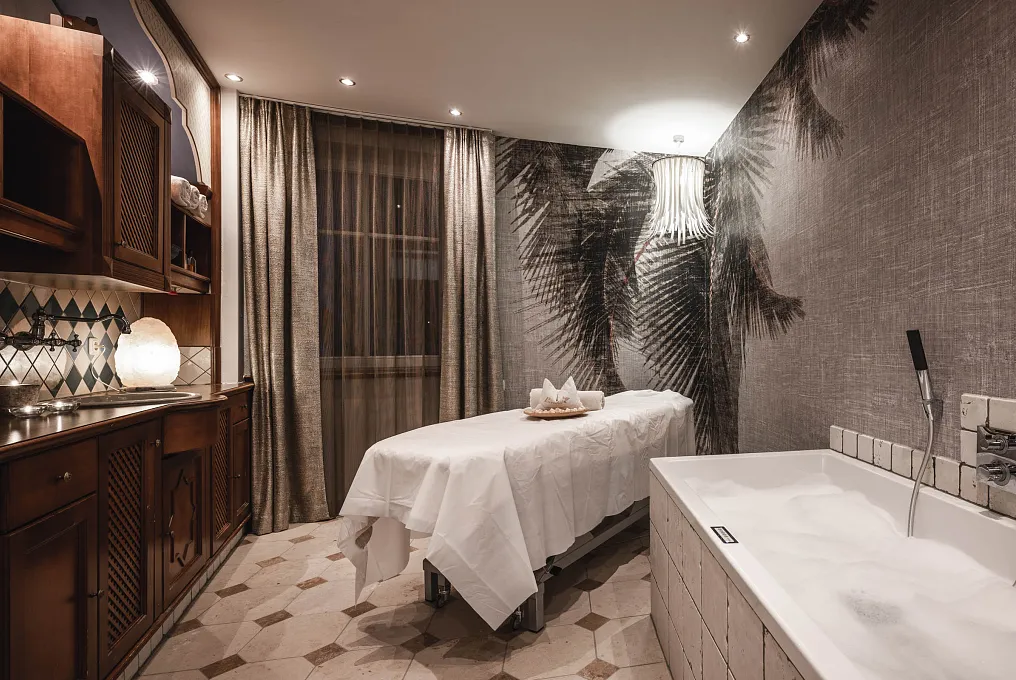 Wellnessraum mit Massageliege, Badewanne und neutraler Dekoration in warmen Tönen.