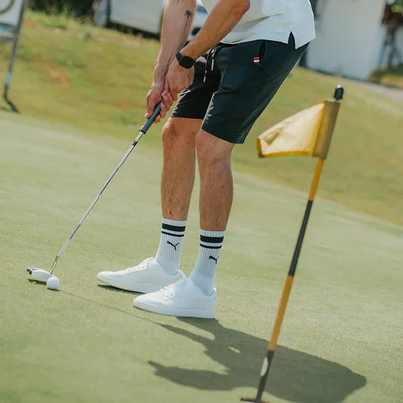 Person beim Golfspielen auf einem Putting Green, mit golfschläger und Fahnenloch in der Nähe.