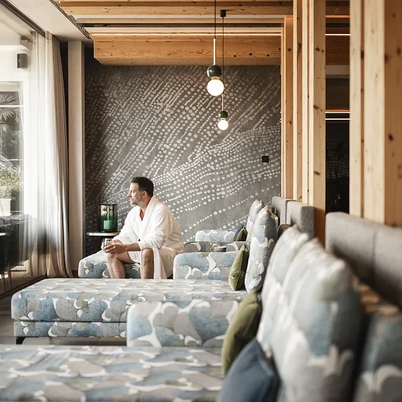 Person im Bademantel sitzt in modernem Lounge-Bereich mit grauer, gemusterter Wand.