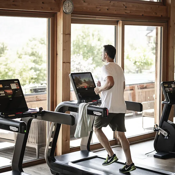 Mann läuft auf einem Laufband in einem hell erleuchteten Fitnessstudio mit großen Fenstern.