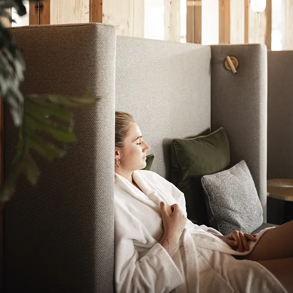 Person relaxing on a modern gray sofa with wooden partitions and plants around.